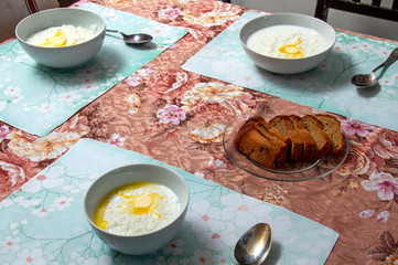 Breakfast. Three white plates with milk porridge with butter. A transparent plate with bread is on the table.
