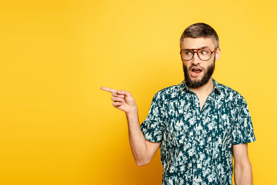bearded guy in glasses pointing with finger aside on yellow