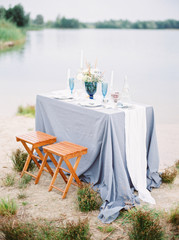 Romantic dinner. Dining table with blue tablecloth and wooden chairs on the beach. Country wedding in blue color.