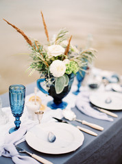 Fine art dinner on a beach. Blue wedding. Catering. Wedding bouquet with tender flowers in vase on table, elegant table setting. Valentine's day dinner idea.