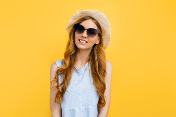 happy girl in summer hat wearing sunglasses in summer clothes smiling on isolated yellow background