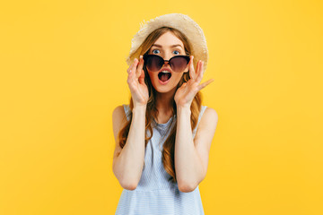 Shocked girl in sunglasses and a summer hat, on a yellow background. Travel, vacation, summer