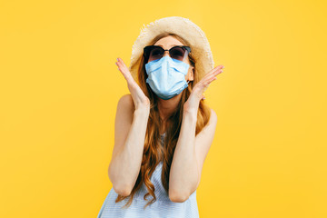 Shocked girl in a summer hat and sunglasses, wears a medical protective mask against a viral infection, on a yellow background. Quarantine, coronavirus, summer