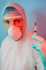 Doctor in protective uniform, reperitor, glasses, gloves on blue background in neon light. close-up portrait of doctor in red neon. tired man is battling coronavirus. syringe with vaccine. covid 19