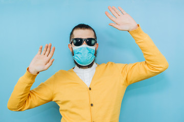 Naklejka premium a man with glasses and a medical mask on a blue background. An emotional and positive guy on self-isolation. Coronavirus. Studio shooting. Pandemic COVID 19.
