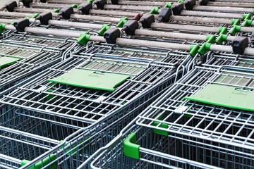Empty metal carts on wheels for food or large size things. A pattern of inserted in each other steel grocery carts, standing under an plastic awning in a shopping center parking lot
