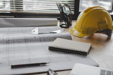 construction working tool, blueprint and yellow safety helmet on architect workplace desk in meeting room office center at construction site, construction, engineering tools and architectural concept