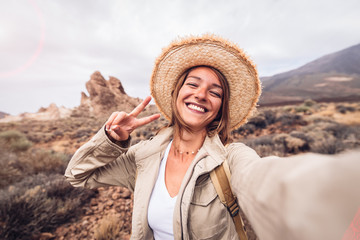 Beautiful happy hiker woman taking a selfie hiking a mountain at vacation. Girl wearing hat and...