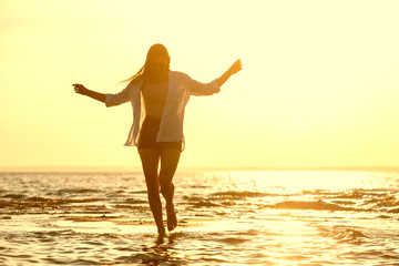 Happy beautiful girl walks at sunset beach in water