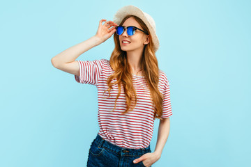 Attractive happy girl in sunglasses and a summer hat, on an isolated blue background