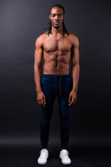 Full body shot of young handsome muscular African man with dreadlocks shirtless