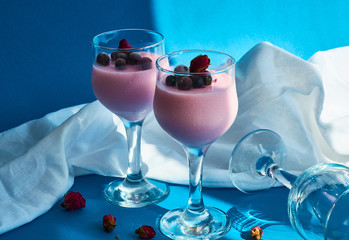 Dessert Panna cotta with currant berries in glasses on  leg is decorated with tea rose on blue background.
