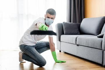 Selective focus of man in medical mask and rubber gloves holding broom at home