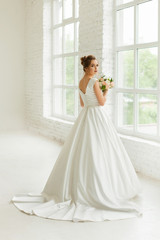 bride in white wedding dress. happy beautiful young woman in white traditional wedding dress on white background. big windows and white walls.