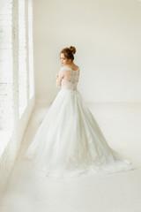 bride in white wedding dress. happy beautiful young woman in white traditional wedding dress on white background. big windows and white walls.