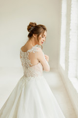 Fototapeta premium bride in white wedding dress. happy beautiful young woman in white traditional wedding dress on white background. big windows and white walls.