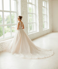 bride in white wedding dress. happy beautiful young woman in white traditional wedding dress on white background. big windows and white walls.