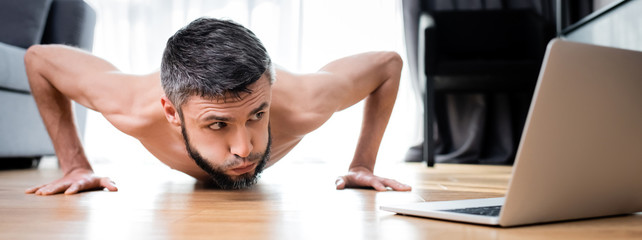 Panoramic crop of shirtless man doing push ups near laptop on floor © LIGHTFIELD STUDIOS