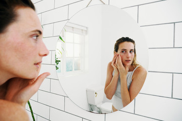 confused beautiful woman looking at herself in the bathroom mirror
