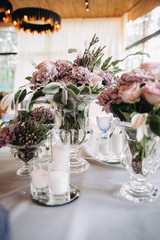 Wedding decor in purple and gray. Banquet tables with tablecloths are decorated with compositions of flowers, on the tables are plates, glasses and candles