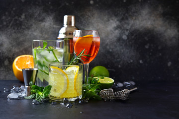 Three classic cocktails : aperol spritz, mojito and lemon cooler with rosemary with ingredients for making and cocktail set. - obrazy, fototapety, plakaty