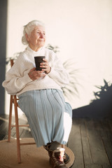 Grandmother is sitting in the chair and drinking tea at home. Beautiful old woman portrait....