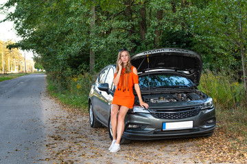 Upset young woman with cell phone near broken car - Image