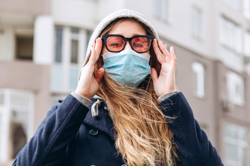 Closeup portrait of a girl in a medical mask on the street, epidemic of a coronavirus. A woman is putting on a mask. The man violated the rules of self-isolation. SARS-CoV-2. Stop COVID-19.