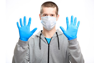 A sports man in a medical mask shows rubber gloves put on his hands, a stop gesture, wearing a sports jacket, staring at the camera. Close-up, isolated