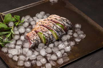 Fresh river fish on metal tray with melting ice. Lemon and sprigs of rosemary.