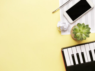 Top view of piano keyboard with sell phone, headphones, note paper and plant on grey background....