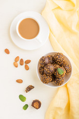 Chocolate caramel ball candies with almonds and a cup of coffee on a white wooden background. top view.