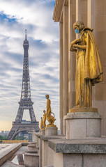 Paris, France - 05 06 2020: Golden statue of a woman wearing a surgical mask during confinement against coronavirus and the eiffel tower
