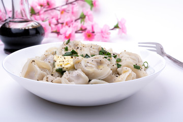 appetizing dumplings in a plate, sprinkled with green onions, with a piece of melting butter, on a white background