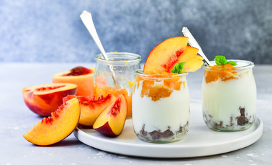 yogurt with peach jam and fresh peaches in a round glass jar on a gray background, dessert recipe. healthy breakfast ,  selective focus