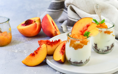 yogurt with peach jam and fresh peaches in a round glass jar on a gray background, dessert recipe. healthy breakfast ,  selective focus