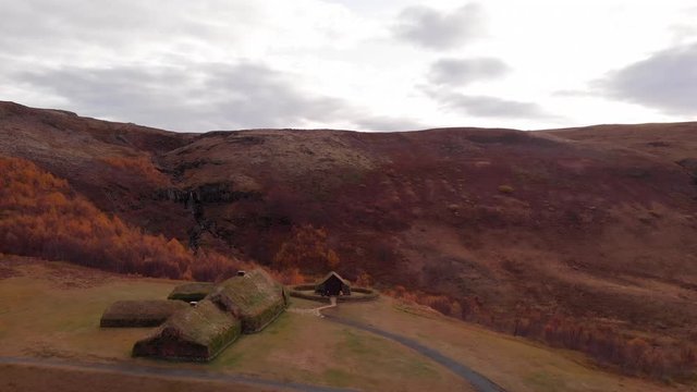 Aerial 4k view of a couple sitting near traditional Icelandic Turf Houses in autumn with a beautiful landscape, Iceland, Europe, reveal shot
