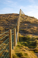 A wire and wood fence leading path up a steep cliff