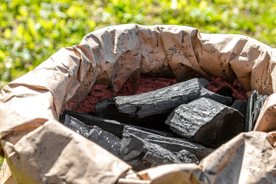 Black charcoal in a paper bag. BBQ season. Black charcoal taken out of the bag with metal pliers.
