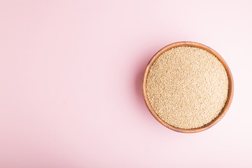 Wooden bowl with raw white quinoa seeds on a pastel pink background.  Top view, copy space.
