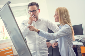 Businesswoman and businessman standing in front of flipchart and presenting graphs during a business meeting in the office.