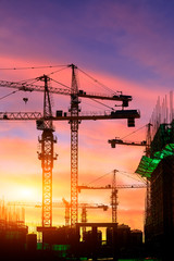Tower crane and building construction site silhouette at sunrise.