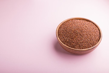 Obraz na płótnie Canvas Wooden bowl with raw red quinoa seeds on a pastel pink background. Side view, copy space.