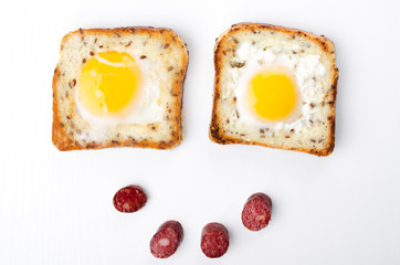 Happy morning and tasty breakfast.Top view of two eggs in the hole adn pieces of fried sausages on the white background
