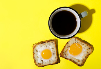 Top view of two slices of bread and fried eggs in it and cup of hot coffee on the yellow background.Traditional breakfast.Empty space
