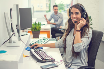 Friendly female helpline operator in call center. Saleswoman in headset using computer in office.