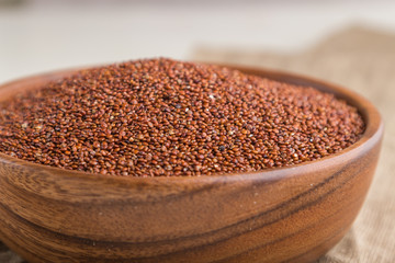 Wooden bowl with raw red quinoa seeds on a white wooden background. Side view, close up, selective focus.
