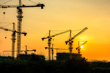 Tower crane and building construction site silhouette at sunrise.