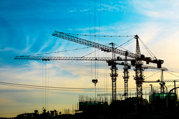 Tower crane and building construction site silhouette at sunrise.