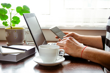 Businessman, freelancer holding pen, using mobile smart phone, working on laptop computer at home